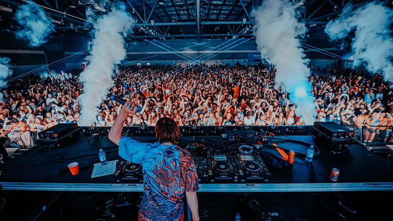 photo of an edm show at the expo center showing the  back of a dj facing a large crowd.