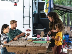 family outside during a camping trip with RV at the background, playing cards at a table.